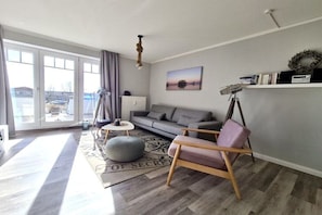 A modern living room with a sofa, armchair, and a view through large windows. - Diek un Düün Zum Böhlerstrand (St.Peter-Ording)