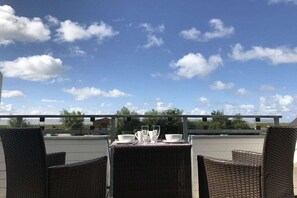 An outdoor dining area with wicker chairs and a table set for two, overlooking a clear sky with clouds. - Diek un Düün Zum Böhlerstrand (St.Peter-Ording)
