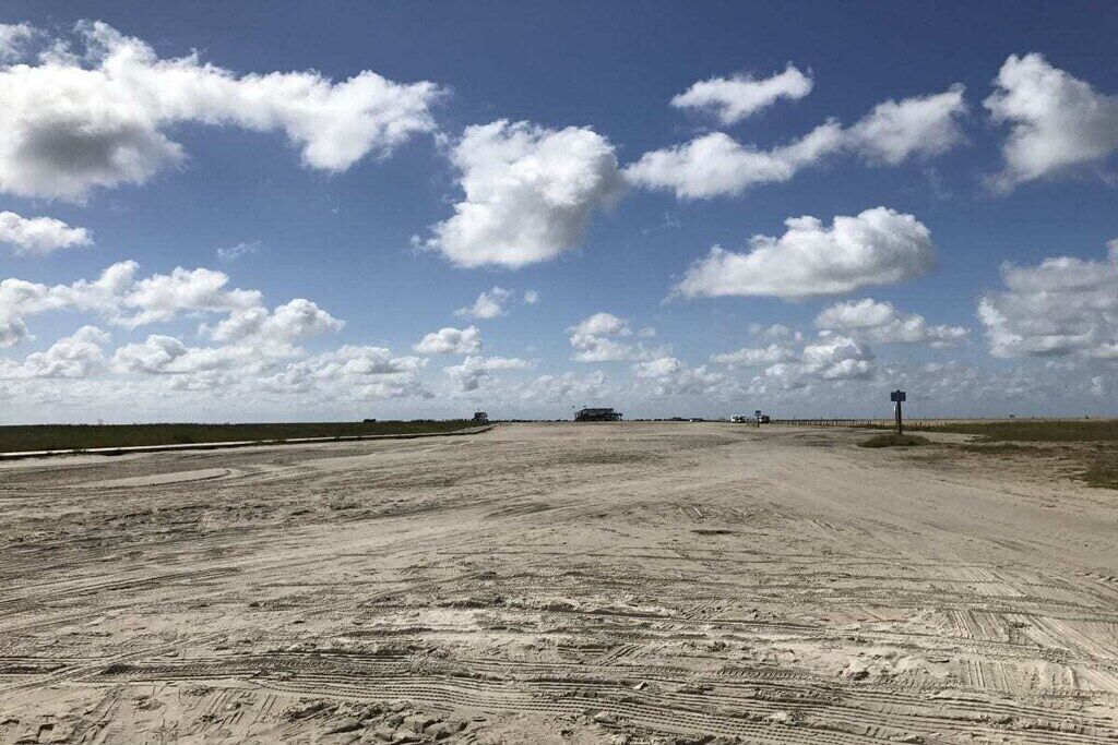 Un camino de tierra ancho y despejado con surcos de neumáticos que conducen a una construcción distante.