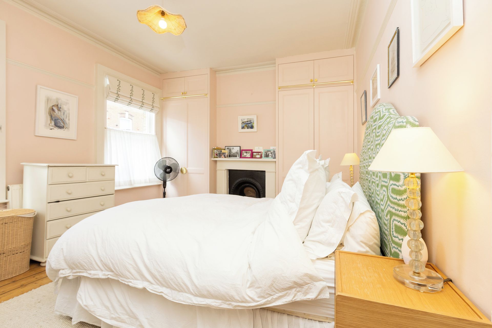 A bedroom with a bed, bedside table, lamp, dresser, and a fireplace.