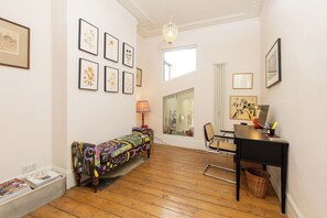 A room with a wooden floor, a desk with a lamp, a chair, a colorful sofa, and framed artwork on the walls. - Stylish 3BDR 2BA House with Garden in East Dulwich (Greater London)