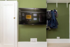 Una habitación con una televisión de pantalla plana montada en una pared verde, una puerta blanca y un perchero con diversos objetos.