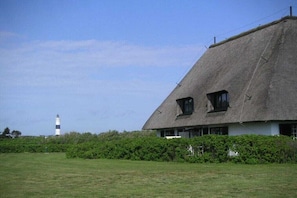 A thatched-roof house with a lighthouse in the background. - Holiday apartment with 1 bedroom (Wenningstedt \/ Sylt)
