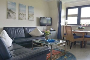 Una sala de estar con sofá, una mesa de centro, televisor de pantalla plana y un comedor con sillas y una mesa.