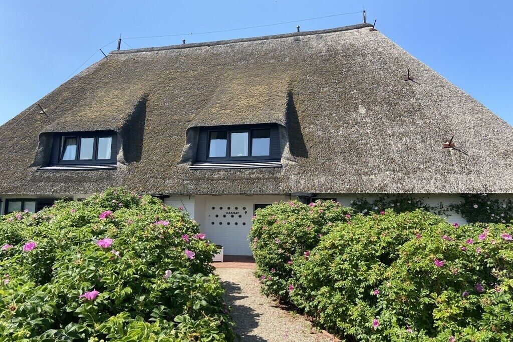 A thatched-roof building with two windows and a pathway leading to it.