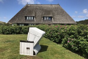 A house with a thatched roof and a garden with pink flowers. - Holiday apartment with 1 bedroom (Wenningstedt \/ Sylt)