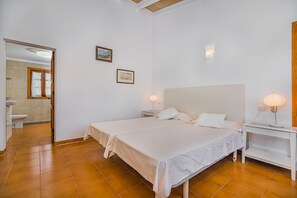 Ein Schlafzimmer mit einem Bett, Nachttischen und einem Schminktisch. Ein Badezimmer ist durch eine geöffnete Tür sichtbar.