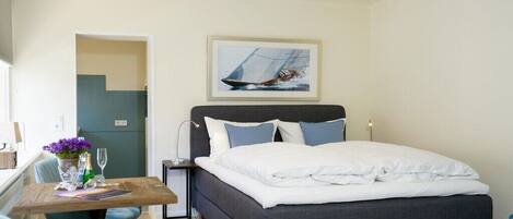 A bedroom with a bed, a desk, a chair, and a painting on the wall.