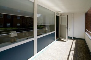 A corridor with a glass door leading to a room, a window with blinds, and a brick wall. - Holiday apartment with 1 bedroom (Westerland)