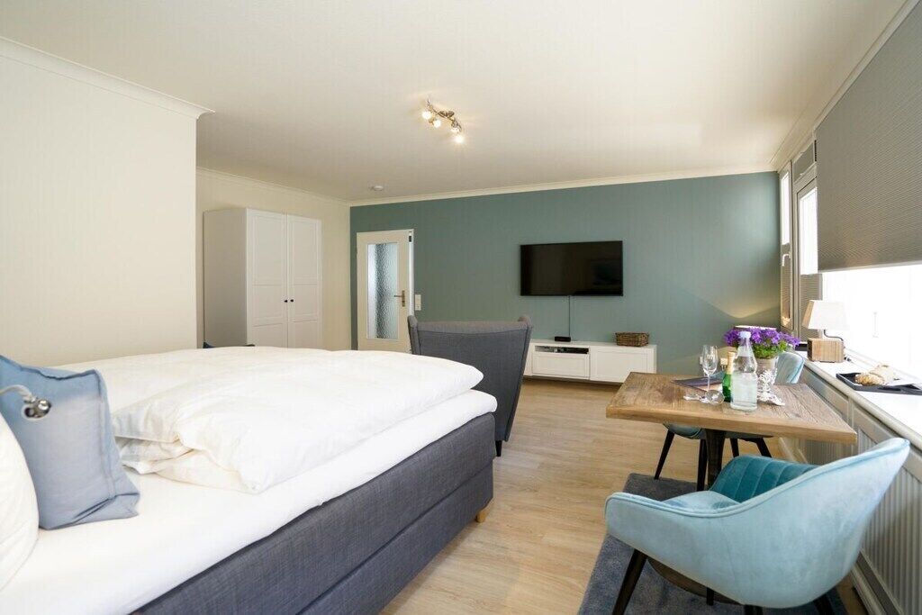 A bedroom with a bed, a desk, a chair, and a television on the wall.