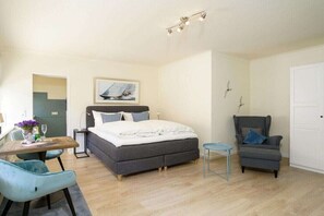 A bedroom with a bed, a desk, two chairs, a small table, and a door. - Holiday apartment with 1 bedroom (Westerland)