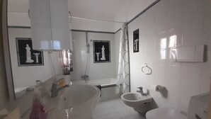 A bathroom with a sink, toilet, and bidet. There are two mirrors, one above the sink and one above the toilet. A shower curtain is visible, and there is a towel rack on the wall. - Vrbo Property (Praiano)