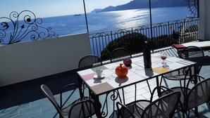 A terrace with a table set for dining, overlooking a body of water and mountains. - Vrbo Property (Praiano)