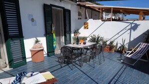 A patio with a table and chairs, a wooden bench, and potted plants. - Vrbo Property (Praiano)