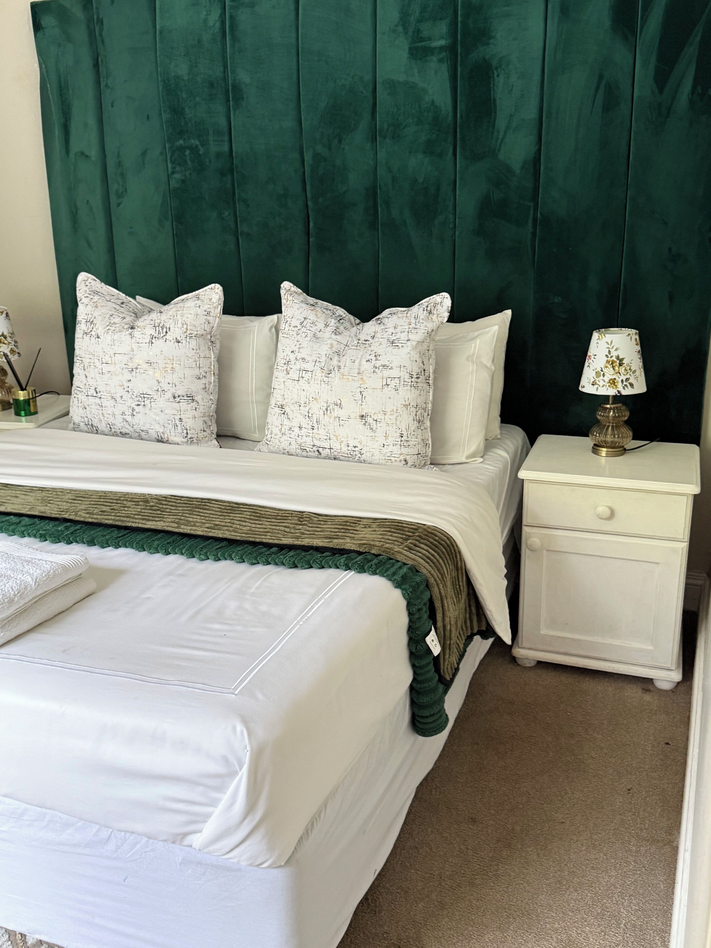 Una cama con ropa de cama blanca, un edredón verde y dos almohadas con estampado blanco y negro.