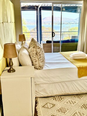 Ein Schlafzimmer mit Bett, Kissen, einer Lampe, Blick ins Freie und einem Fenster.