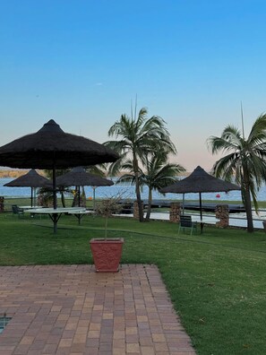 Eine Terrasse am Strand mit Reetsonnenstühlen, Palmen und einem Pflasterweg.