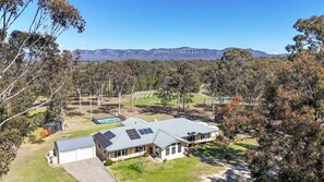 A residential property with a large house featuring solar panels, a swimming pool, and a view of distant mountains. - North Peak Manor - Spacious home with room for everyone (Pokolbin)