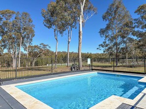 A swimming pool with a surrounding fence, trees, and a clear sky. - North Peak Manor - Spacious home with room for everyone (Pokolbin)