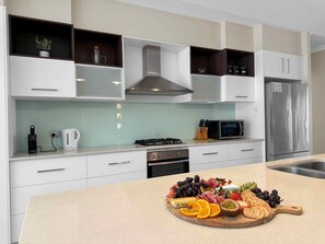 A modern kitchen with white cabinetry, a stainless steel refrigerator, a microwave, and a gas stove. - North Peak Manor - Spacious home with room for everyone (Pokolbin)