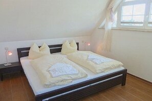Ein Schlafzimmer mit einem Bett, Kissen, einem Nachttisch und einem Fenster.
