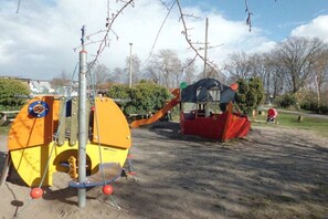 Ein Spielplatz mit verschiedenen Spielgeräten, darunter eine gelb-rote Klettervorrichtung, eine Rutsche und eine Schaukel.