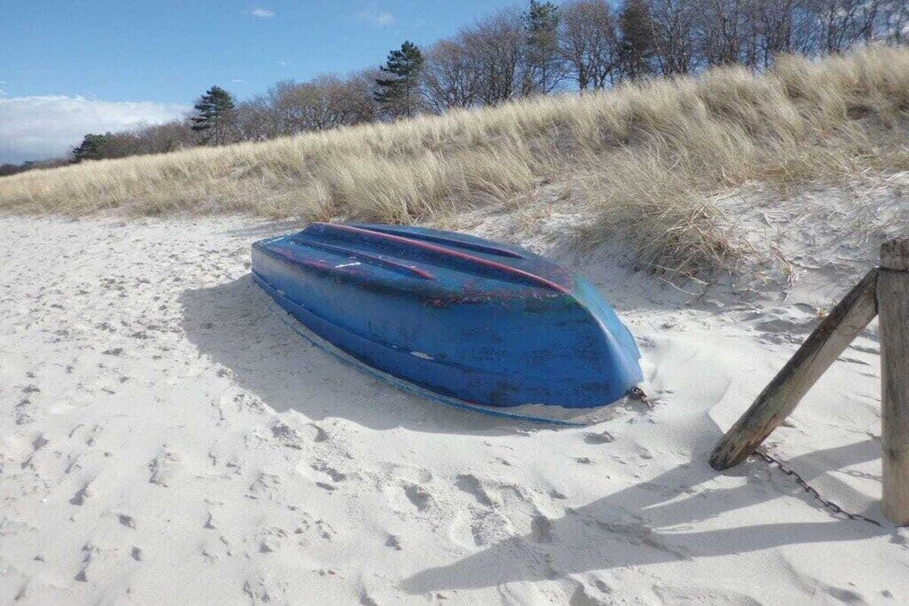 A blue boat on a sandy beach with a wooden post nearby.