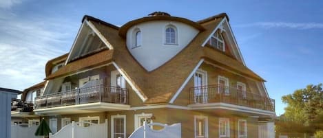 A two-story house with a unique triangular roof design, a balcony on the upper floor, and a gated driveway.