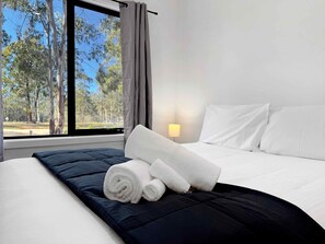 A hotel room with a bed, a window with a view of trees, and a lamp on the nightstand.