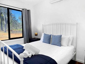 Una camera da letto con un letto, cuscini, un comodino, una lampada e una finestra con tende.