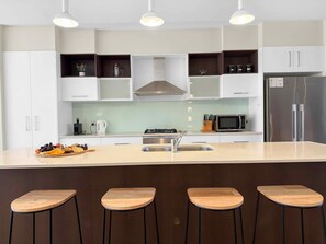A modern kitchen with a central island, bar stools, a stainless steel refrigerator, and a microwave.
