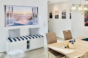 A modern interior with a wooden dining table, cushioned seating, a bench with storage, and a wall-mounted artwork depicting a beach scene. - Holiday apartment with 2 bedrooms (Wustrow)