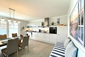 A modern kitchen with white cabinets, a dining table with chairs, and a built-in bench. - Holiday apartment with 2 bedrooms (Wustrow)