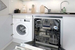 A compact kitchen with a built-in washer and dishwasher, a sink with a soap dispenser, and a small countertop with kitchen utensils.