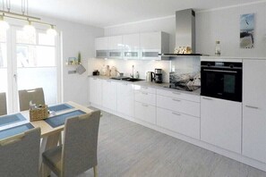 Une cuisine moderne avec des meubles blancs, une table à manger avec des chaises et une machine à café.