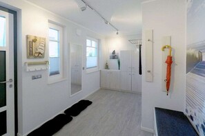 Un intérieur moderne avec un couloir menant à une pièce, des murs blancs, un tapis noir et une porte sur laquelle est accroché un parapluie orange.
