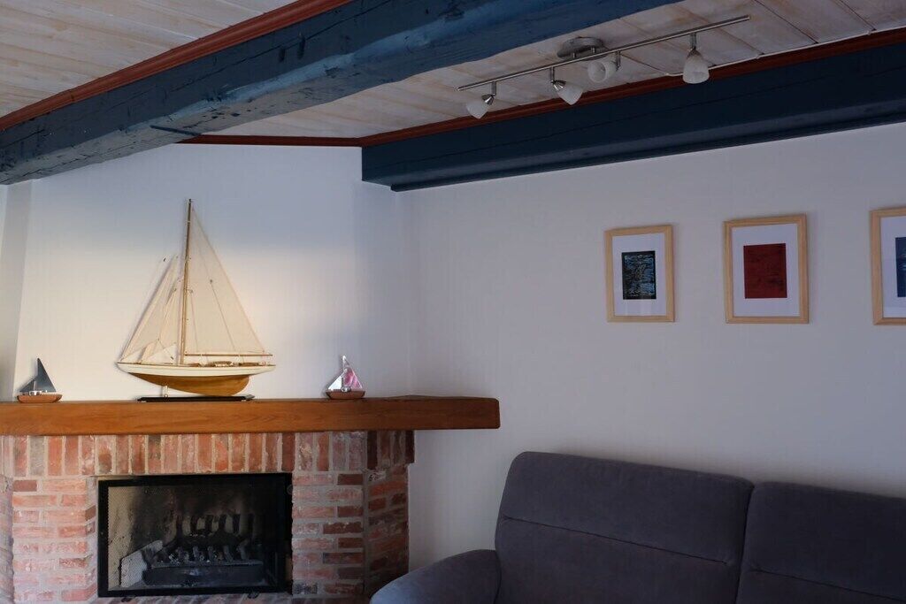 A room with a brick fireplace, a wooden mantel, and a sailboat model. There are framed artworks on the wall.