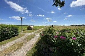 A rural landscape with a gravel path, a stone wall, and a field with hay bales. - Hahnenhof Föhr Apartment 9 (Wrixum)