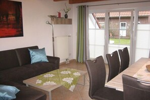 A living room with a sofa, coffee table, and dining area with chairs. - Living Experience GbR (Butjadingen)