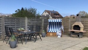 Een terras met een tafel en stoelen, een gestreept voorwerp met een doek en een stenen oven.