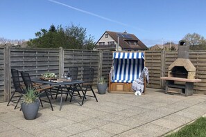 A patio with a table and chairs, a striped cloth-covered item, and a stone oven. - Holiday apartment with 1 bedroom (Maasholm)