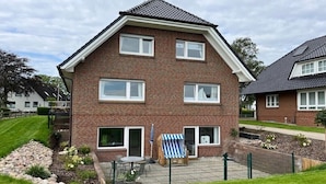 Een twee verdiepingen tellend bakstenen huis met een omheinde achtertuin, een klein terras met een tafel en stoelen, en een blauw-witte gestreepte strandstoel.
