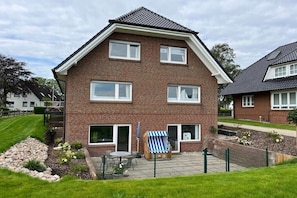 A two-story brick house with a fenced backyard, a small patio with a table and chairs, and a blue and white striped beach chair. - Holiday apartment with 1 bedroom (Maasholm)