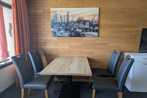 Ein Essbereich mit einem Holztisch und Stühlen, einem Gemälde eines Hafens an der Wand und einem Fenster mit Vorhängen.