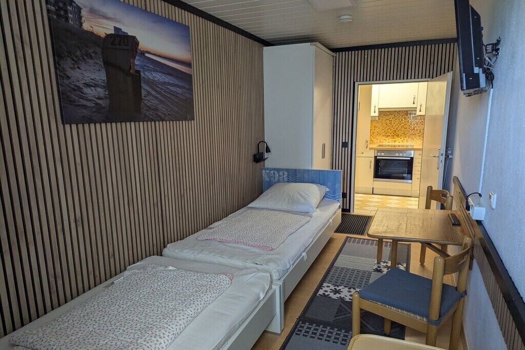 Habitación pequeña con dos camas individuales, una mesita y una silla.