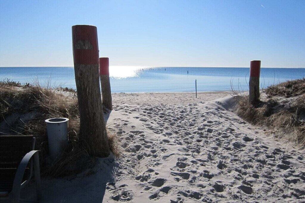 A sandy beach path leading to the sea with wooden posts and a metal pipe.