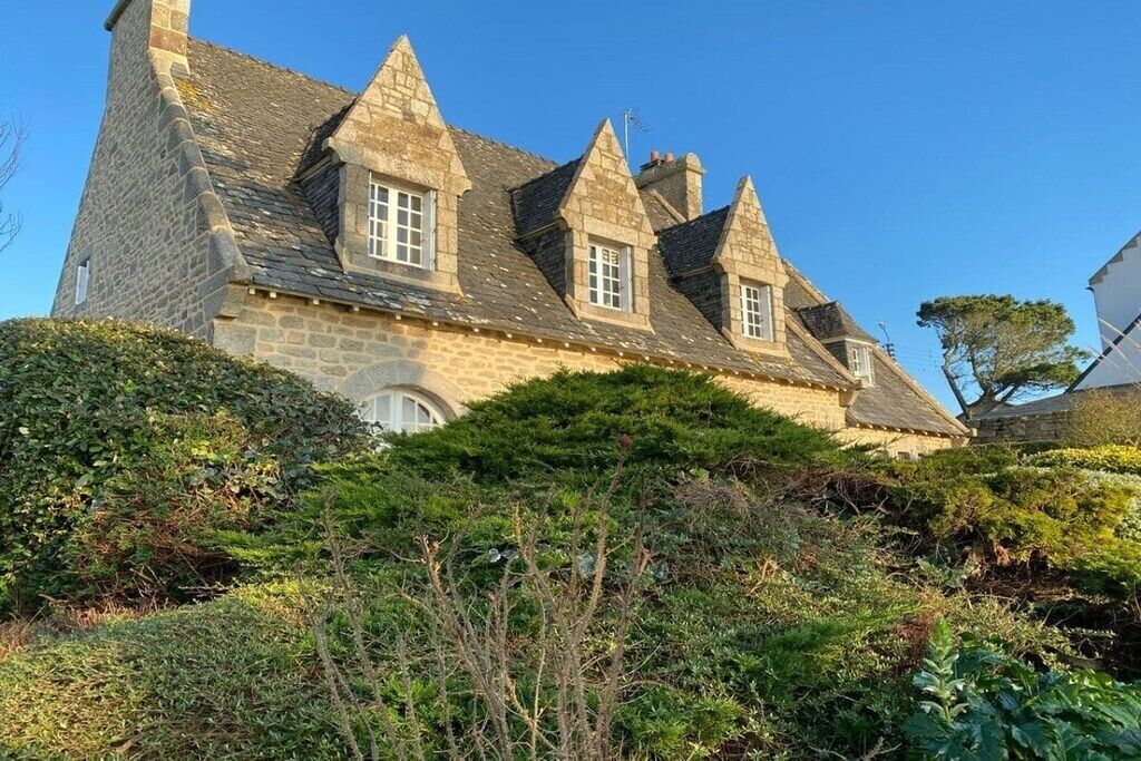 Un bâtiment en pierre doté de plusieurs toits à pignons et d’une cheminée centrale bien visible.