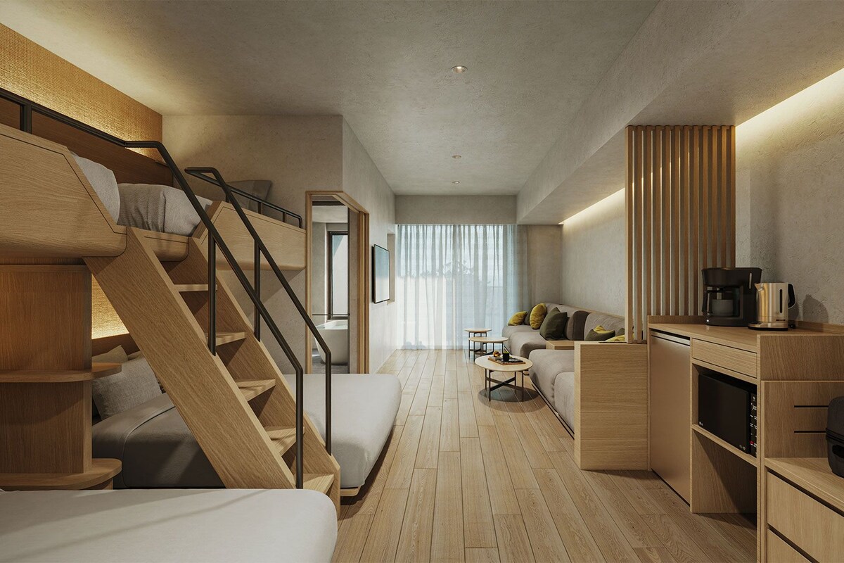 Ein moderner, kompakter Wohnraum mit einer Holztreppe, einer Couch, einem kleinen Tisch und einer Kaffeemaschine.