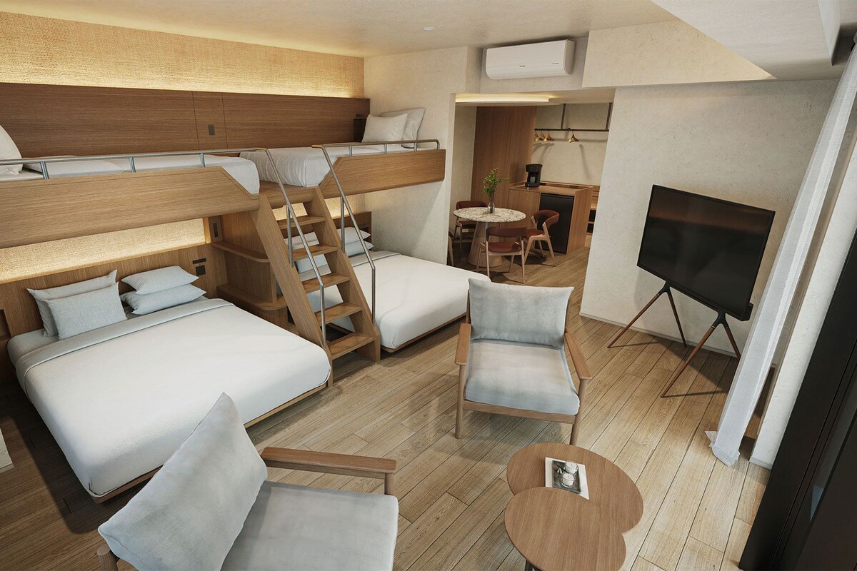 Ein kleines Hotelzimmer mit Etagenbetten, einer Sitzecke, einem Fernseher und einem runden Tisch mit Tablett.