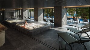 Un área de spa con jacuzzis y sillas reclinables, amplias ventanas con vistas al exterior.